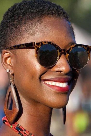 image of a black woman with very short natural hair smiling wearing sunglasses and wooden earrings