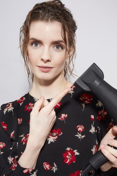 brunette with wet hair pointing at hairdryer