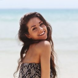 sea salt spray: brunette model at the beach with long wavy beach hair smiling over her shoulder