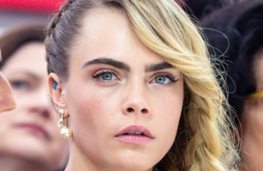 Side hairstyles: Cara Delevingne at Paris Fashion Week AW19 with long blonde hair in a side braid, wearing a pink dress
