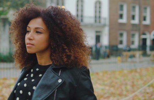 a woman with long curly hair standing outside wearing a leather black jacket