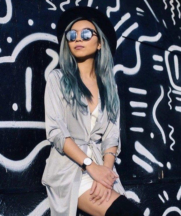 woman with long wavy ice blue metallic denim hair colour leaning against a black and white art wall with black hat and tinted sunglasses