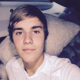 Justin Bieber talking a selfie wearing a white tshirt with a side swept man fringe in his brown hair