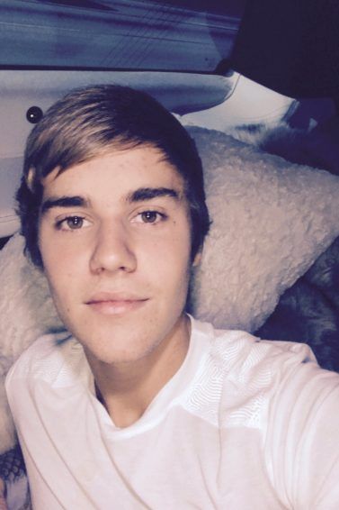 Justin Bieber talking a selfie wearing a white tshirt with a side swept man fringe in his brown hair