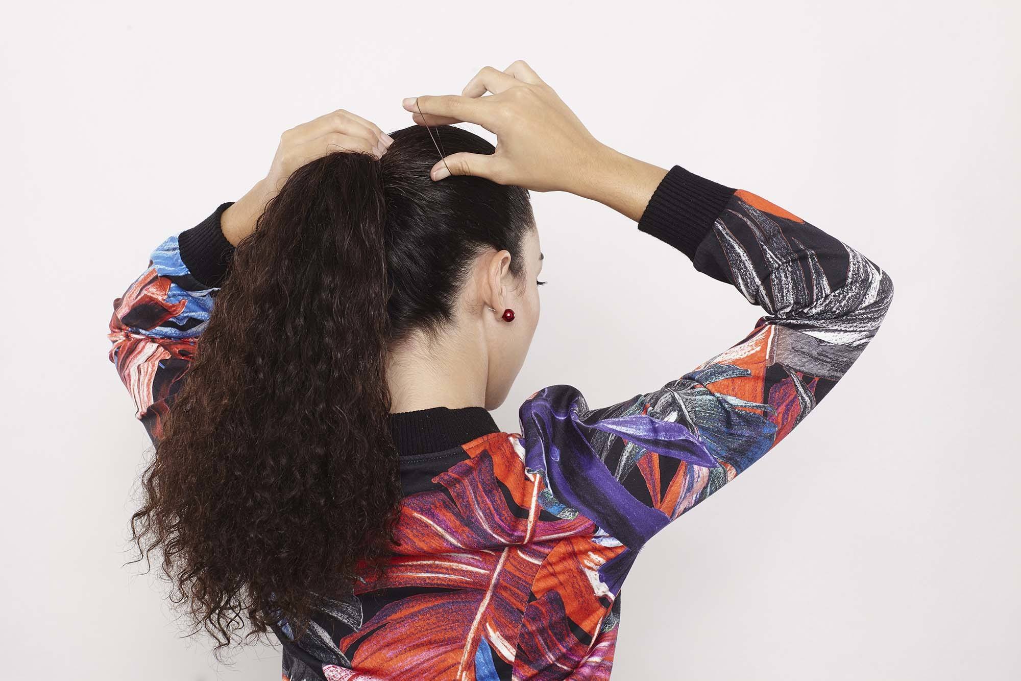 A brunette model tying her long curly hair with an elastic hairband