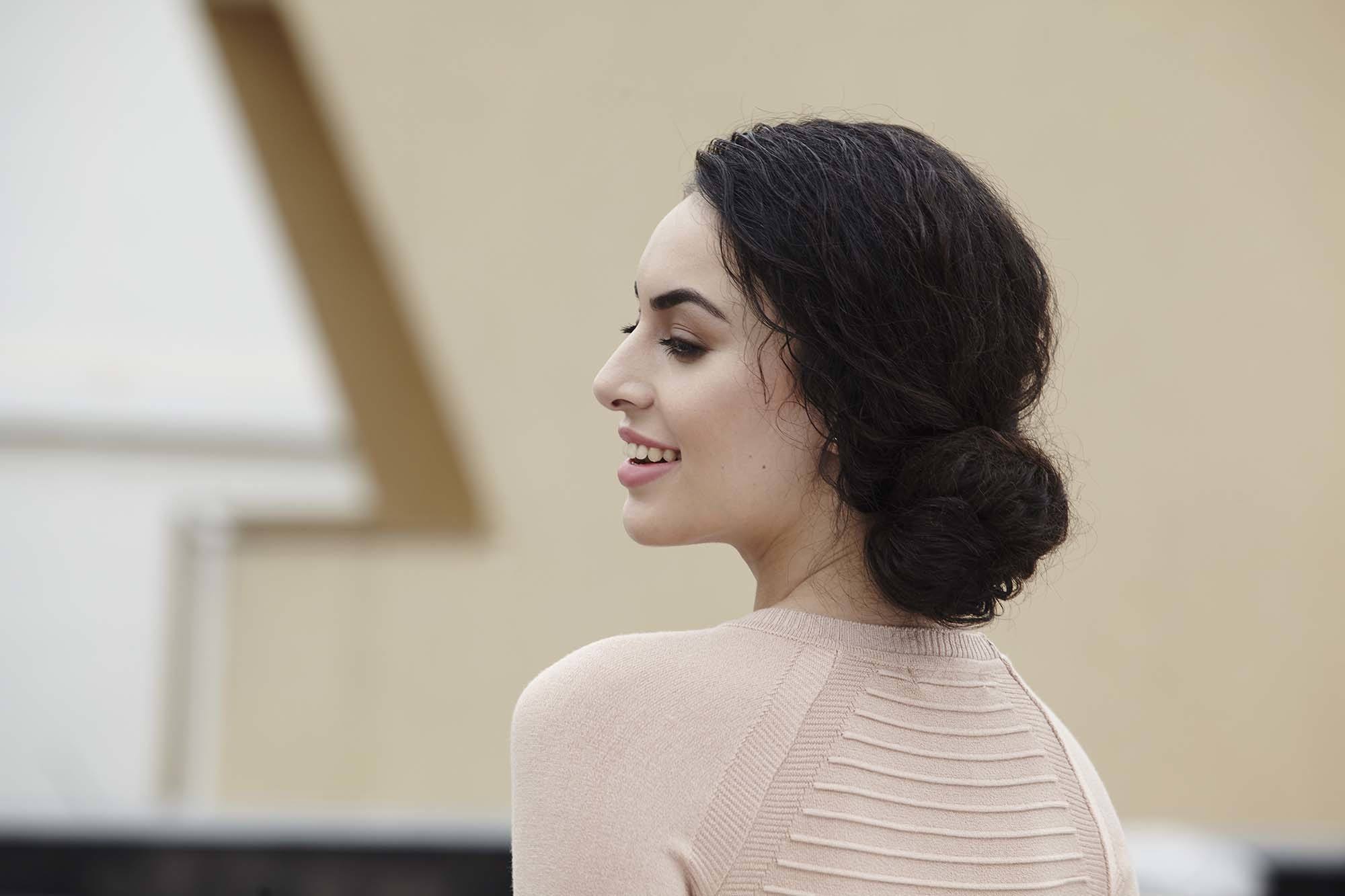 A brunette young woman with her long curly hair put into a low bun