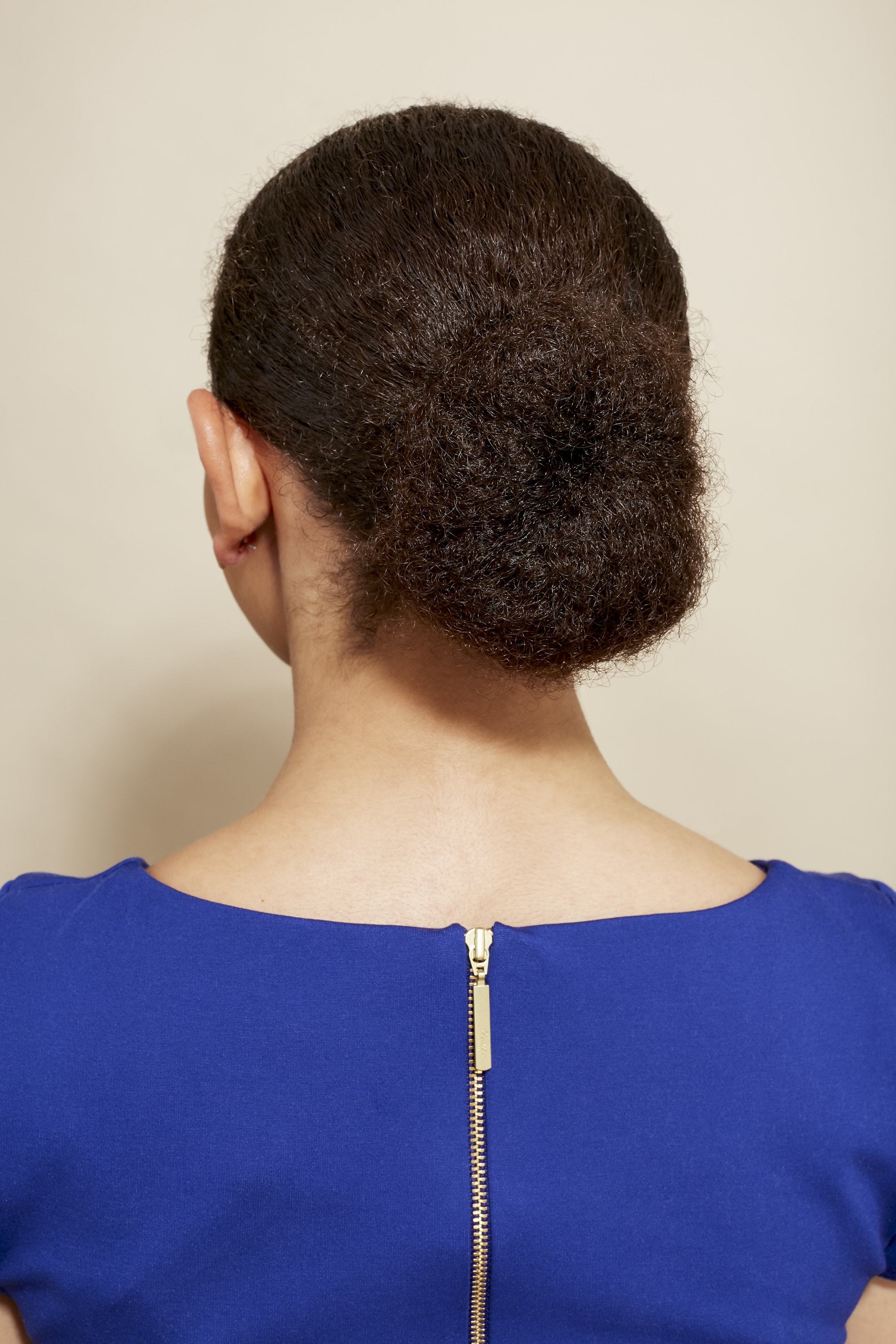 mixed race hair: close up back shot of a woman with natural medium brown hair styled into a smooth low bun, wearing a blue dress and posing in a studio setting