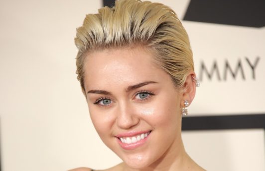 miley cyrus on the red carpet with short blonde hair swept back wearing a plunging neckline black dress