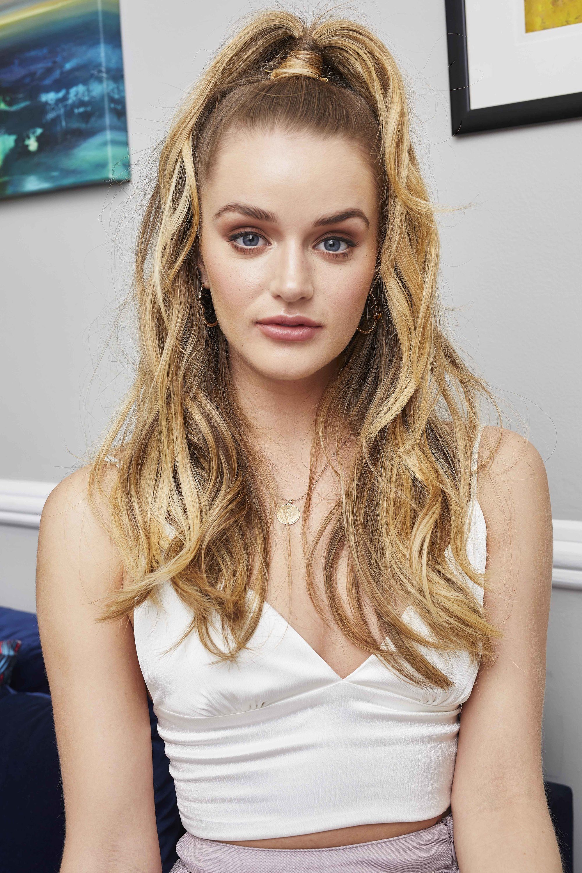 Prom hairstyles: Woman with long wavy blonde highlighted hair in a half-up half-down ponytail wearing a white camisole top