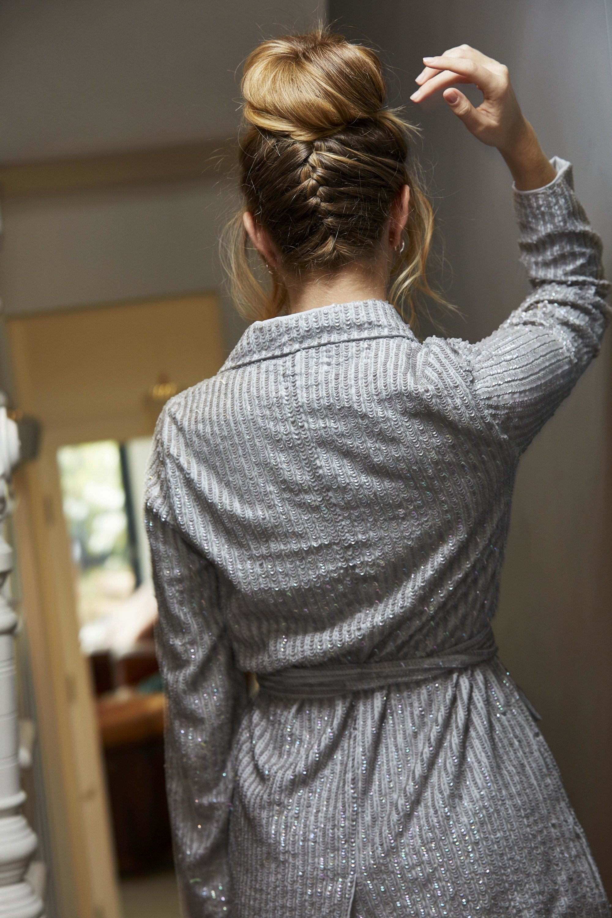 Prom hairstyles: Woman with long dark blonde highlighted hair in a upside down braid bun wearing a grey blazer dress.
