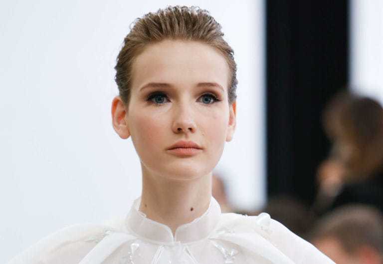 Prom hairstyles: Woman with dark blonde hair in quiff updo wearing white dress.