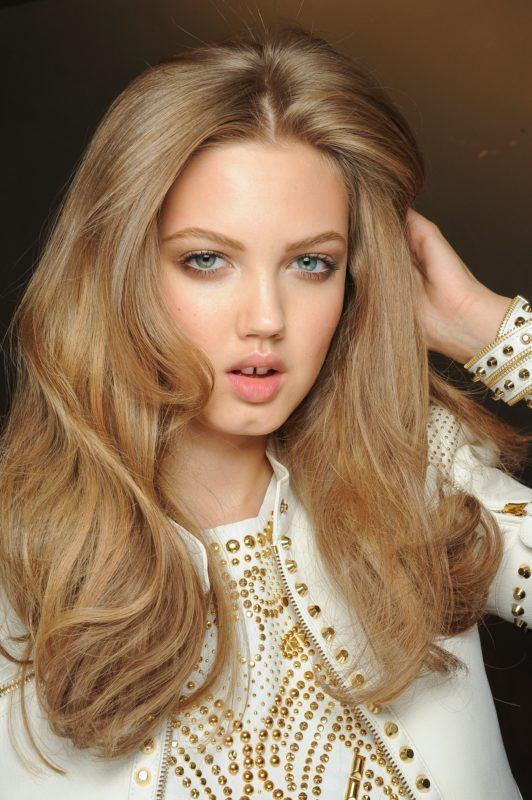 Prom hairstyles: Woman with honey blonde big bouncy blow dried hair wearing a white and gold studded top