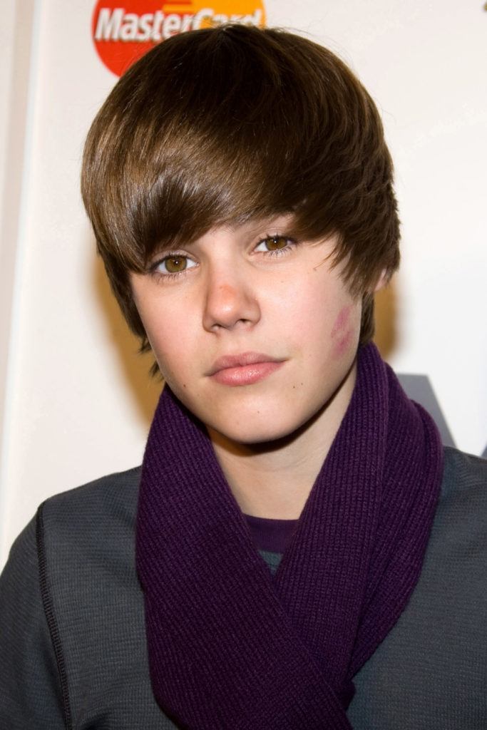 young justin bieber on the red carpet wearing a dark outfit with a purple scarf and his dark brown hair styled into a sweeping fringe