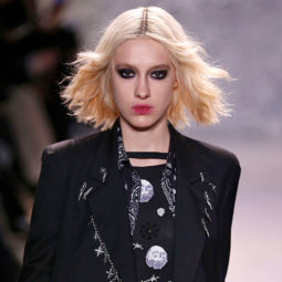 '90s grunge hairstyles on model with blonde wavy bob wearing a black top and green trousers