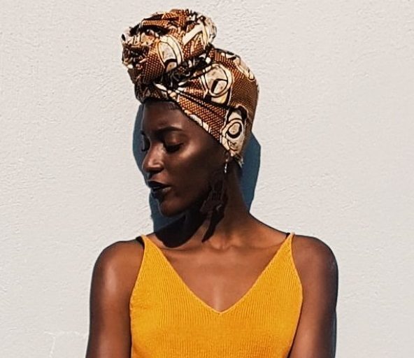 close up shot of woman with head scarf wrapped around her short hair, wearing yellow top and posing outside