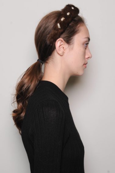 side view of a brunette model backstage at the Altuzarra fashion show wearing a black top with her hair pulled back into a ponytail and a headband