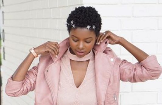 close up shot of woman with fluffed out short natural hair, wearing stars in her hair and all pink outfit, posing outside