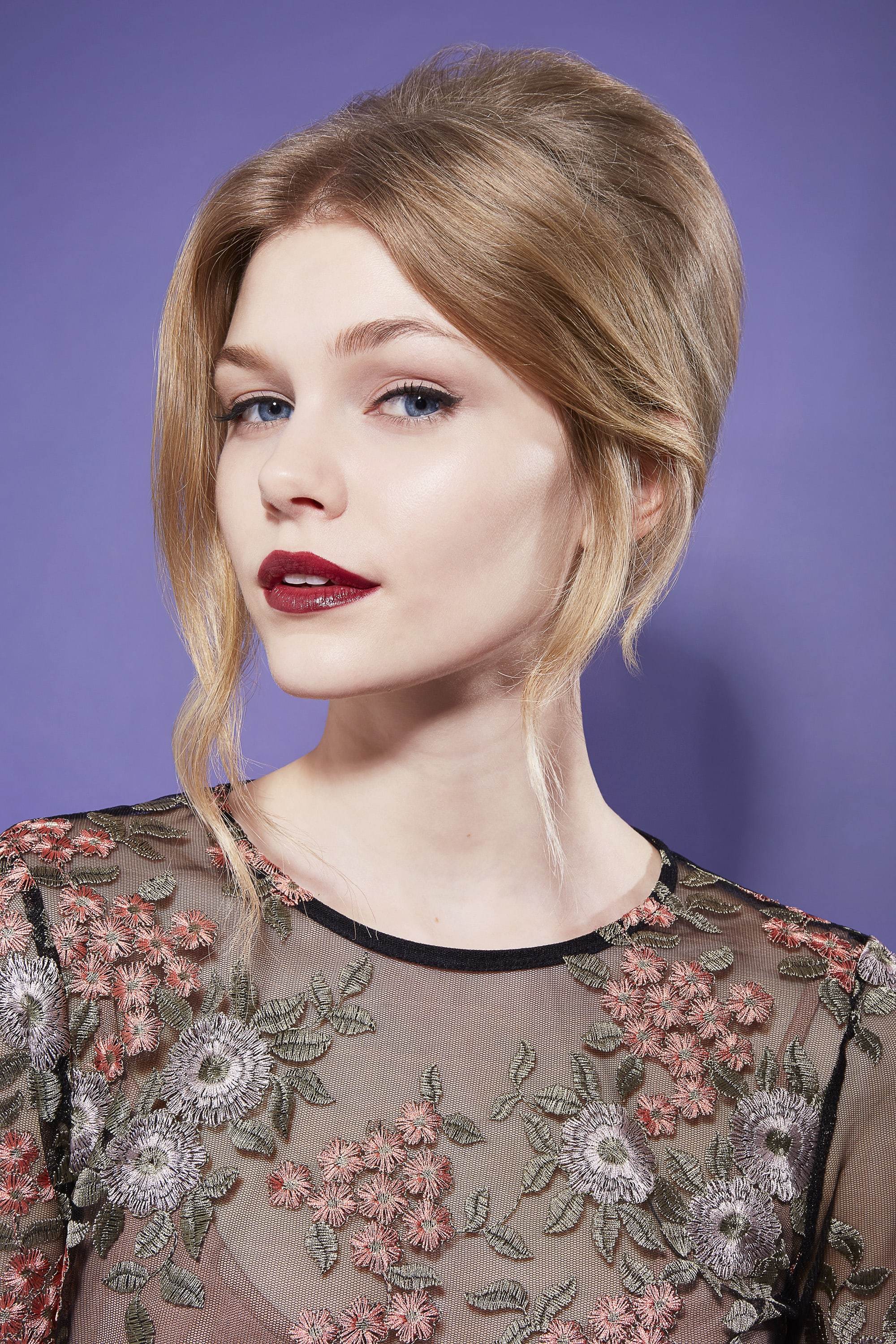 close up shot of model with romantic beehive updo hairstyle, wearing dark purple lipstick and floral top