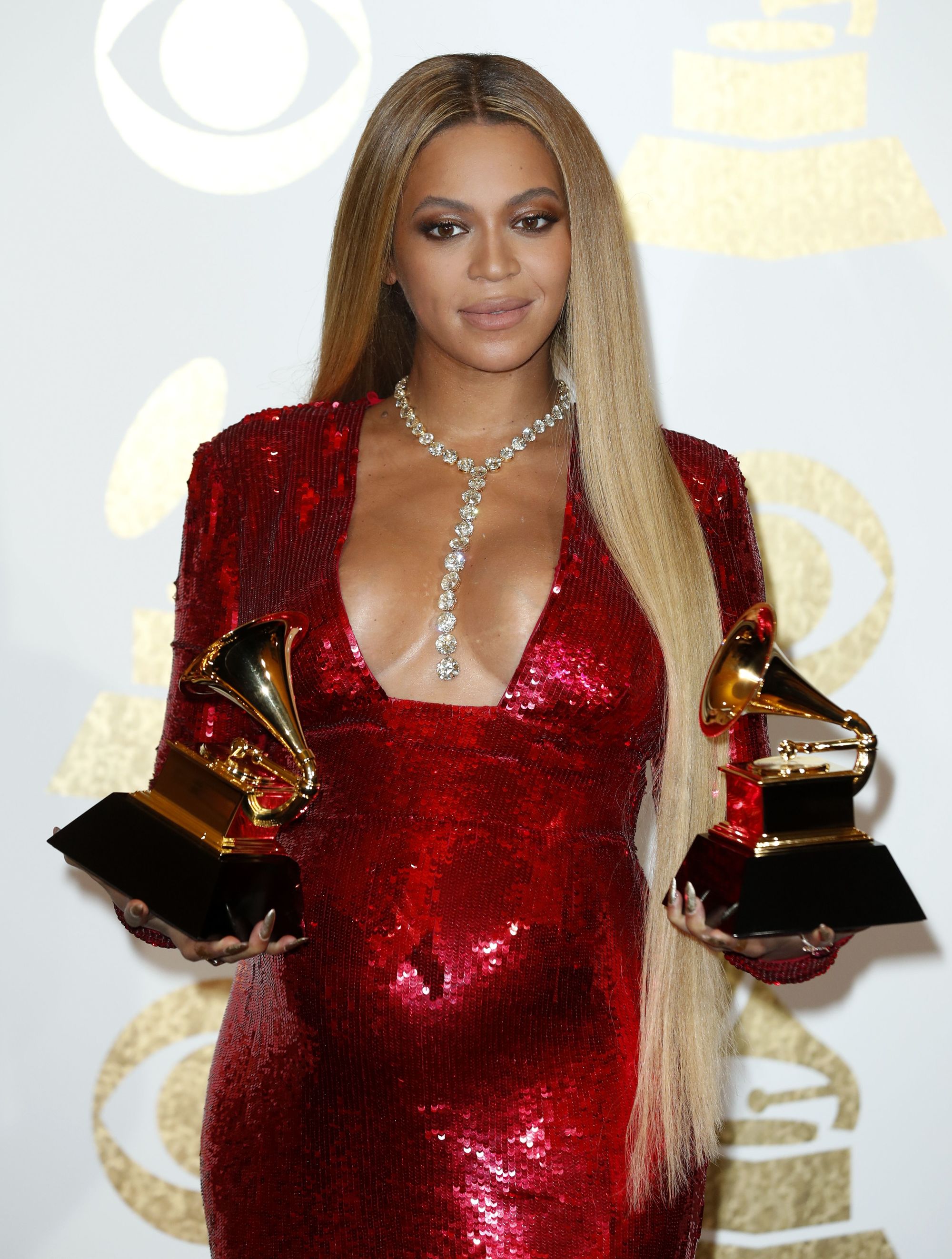 pregnant beyonce on the red carpet in a glittery red sequin dress holding two grammy awards with really long straight blonde hair