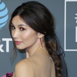 Shot of Gemma Chan with her dark brown hair styled into a braided ponytail with ribbon, wearing purple dress on the red carpet