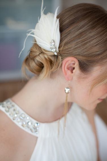 blonde bride with halterneck white dress and a bun hairstyle with feather accessory