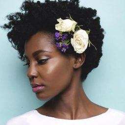 close up shot of woman with short natural hair with flowers in it, wearing white and posing in a studio
