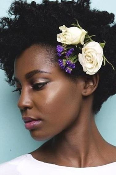 close up shot of woman with short natural hair with flowers in it, wearing white and posing in a studio