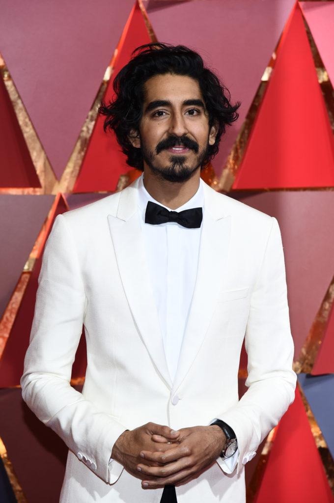 lions actor dev patel with curly hair and white suit and black bow tie