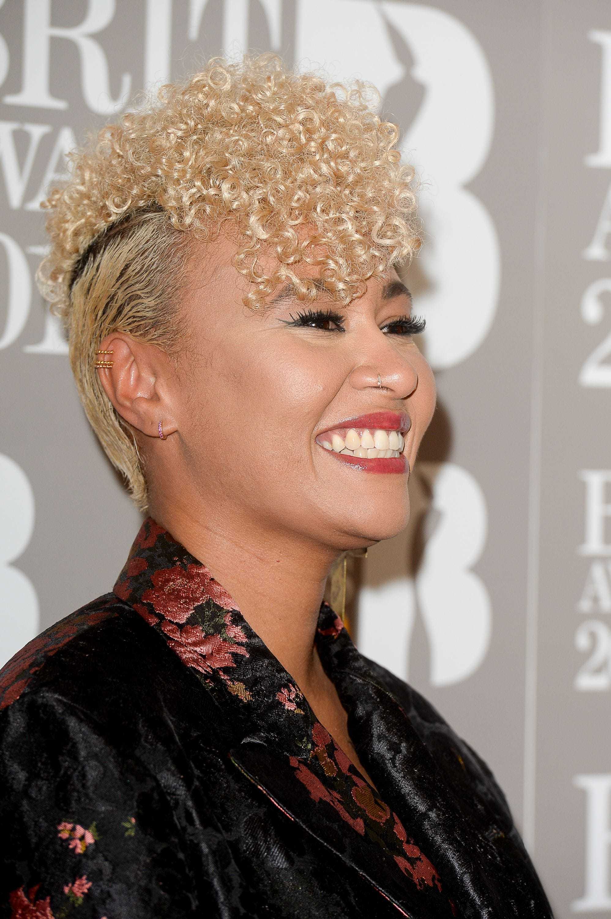 close up shot of Emeli Sande curly fauxhawk hairstyle, wearing black and floral suit and posing on the brit awards 2017 red carpet