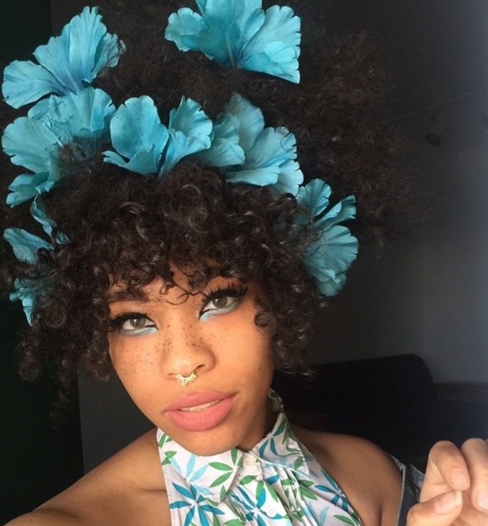 flower hairstyles for afro hair: close up shot of woman with natural curly hair styled into an updo with blue fake flowers in it
