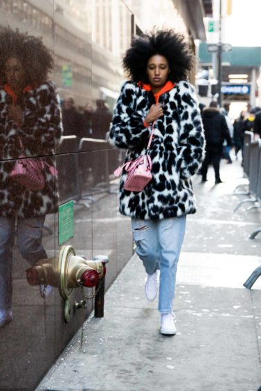 nyfw street styler wearing a spotty animal print fur coat, an orange hoodie, mom jeans and converse with voluminous natural afro hair