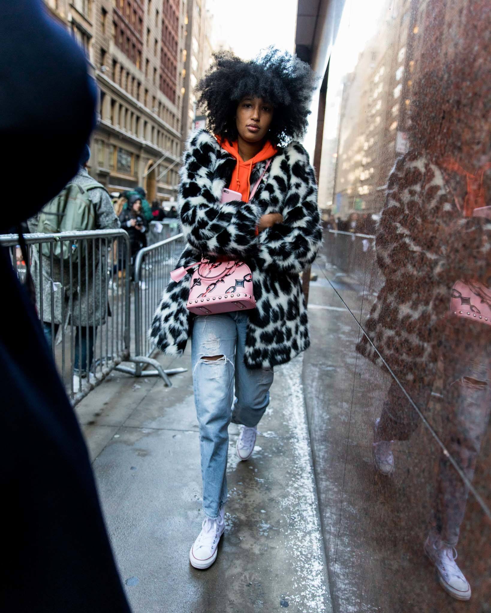 nyfw street styler with long natural hair wearing an animal print fur coat, an orange hoodie and mom jeans with converse