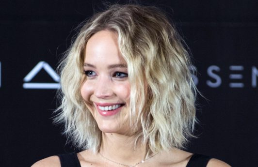 jennifer lawrence on the red carpet in a black v neck dress with blonde curly short bob hair