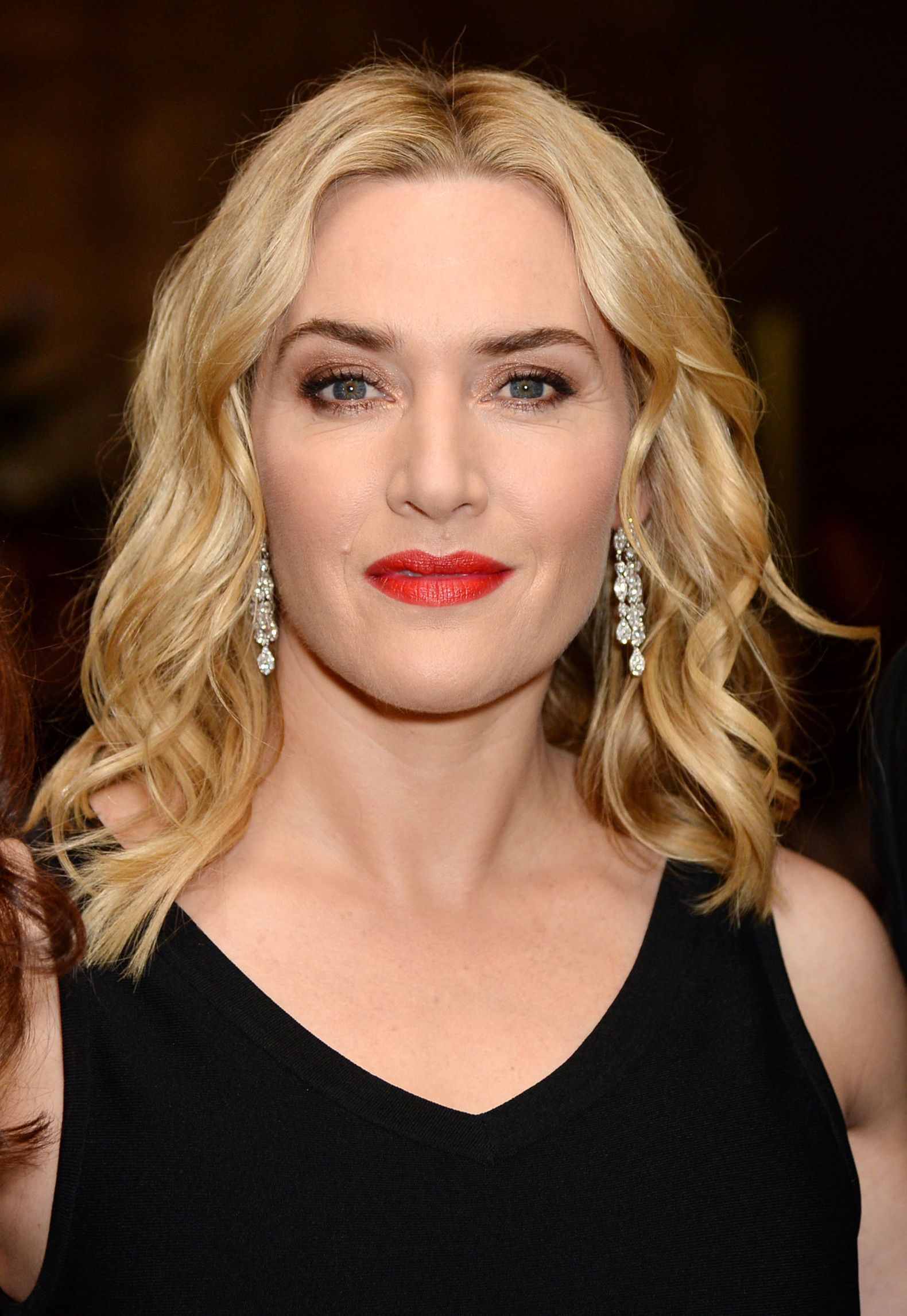 kate winslet in a black v neck dress with shoulder length blonde wavy hair