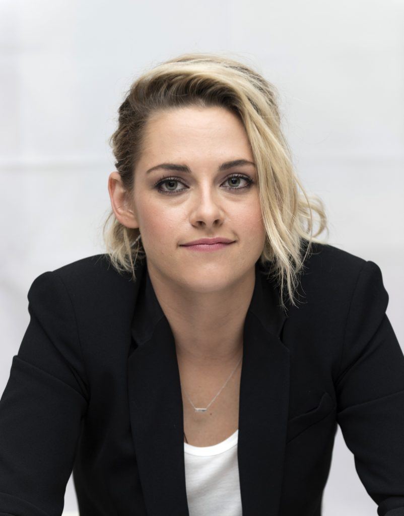 kristen stewart wearing a white top and black blazer with blonde short hair and dark roots