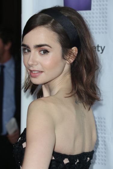 lily collins wearing a strapless black dress with her brunette hair in a bouffant style with a black headband