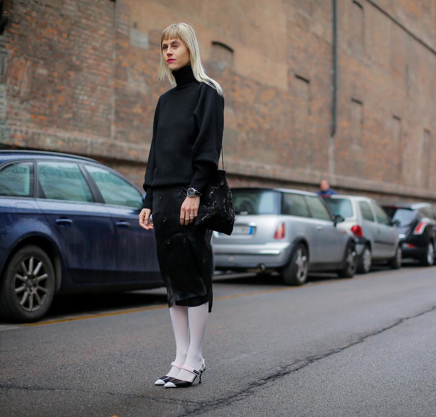 woman with bleach blonde straight hair and micro fringe in street style image wearing white tights, midi skirt and roll neck