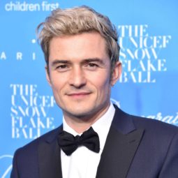 orlando bloom on the red carpet wearing a navy suit with a white shirt and a bow tie and his blonde hair worn in a quiff