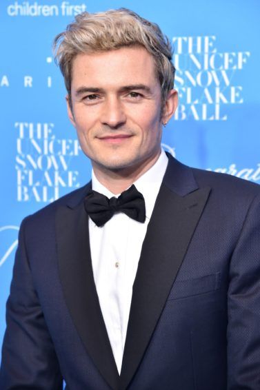 orlando bloom on the red carpet wearing a navy suit with a white shirt and a bow tie and his blonde hair worn in a quiff
