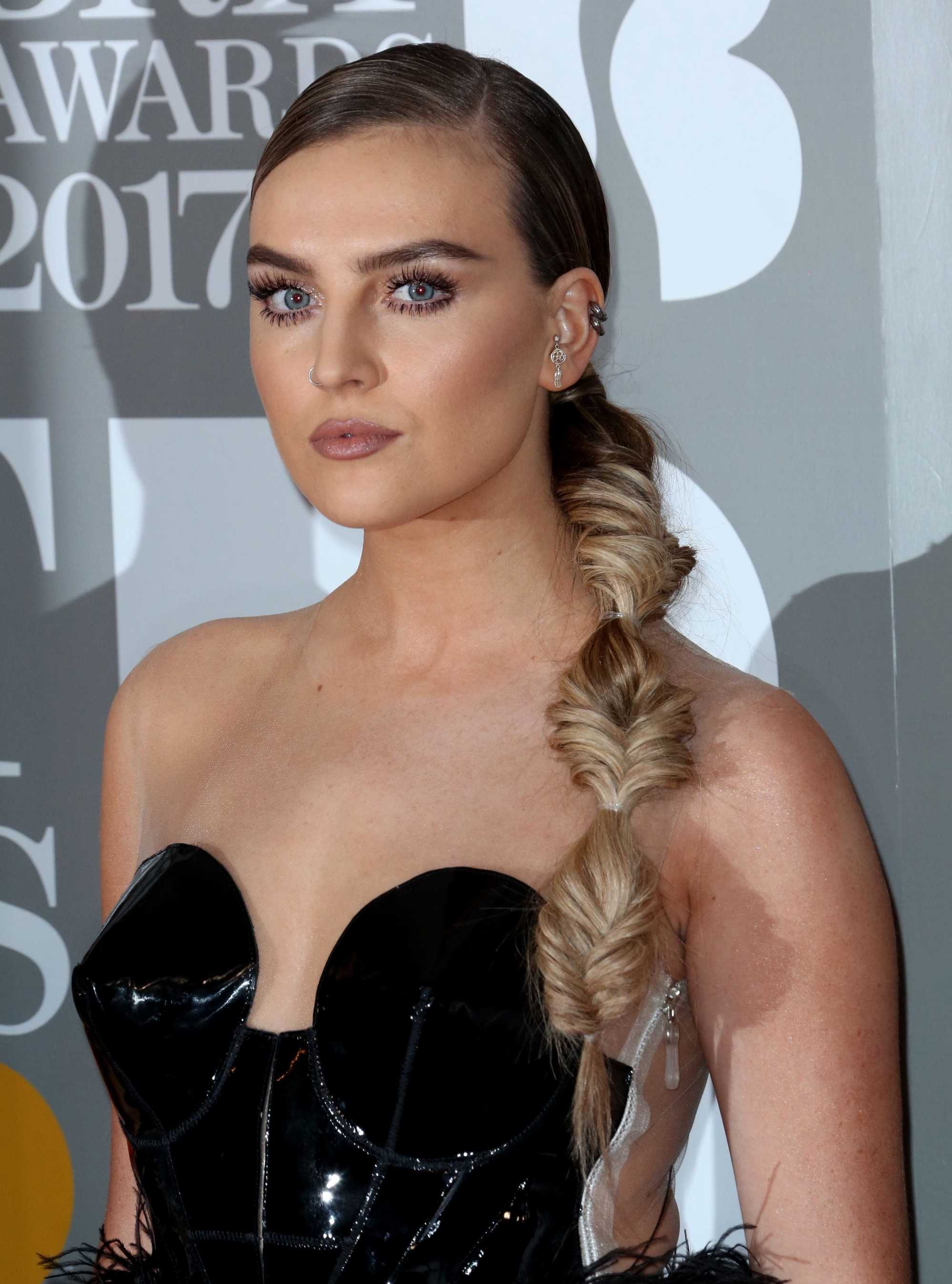 close up shot of Perrie Edwards with long hair fashioned in a side ponytail fishtail braid, wearing black latex on the brit awards 2017 red carpet