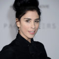 sarah silverman wearing a black pussybow blouse with her black hair styled into a doughnut top knot