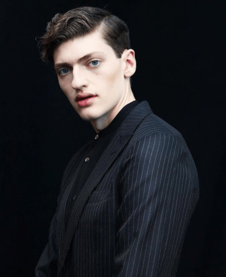 front view image of a man with his hair in a quiff style wearing a black suit