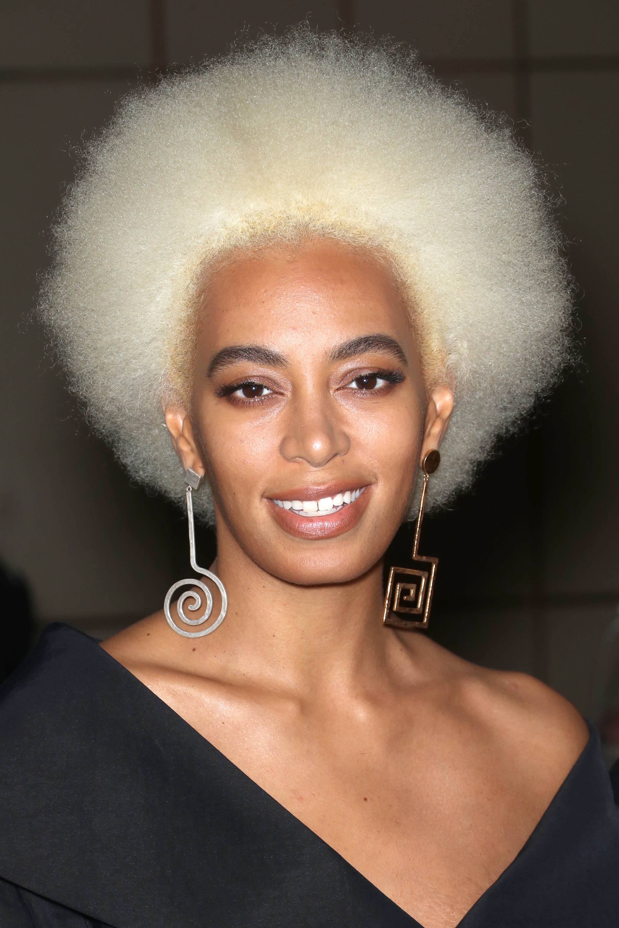 natural hairstyles for short hair: close up shot of solange with blonde afro hairstyle, wearing statement earrings and black outfit, posing on the red carpet