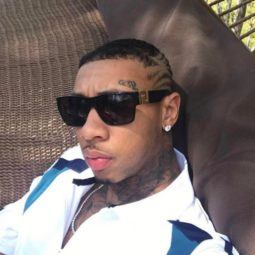 Rapper Tyga taking a selfie wearing a white outfit and dark sunglasses with his hair cut into stripes