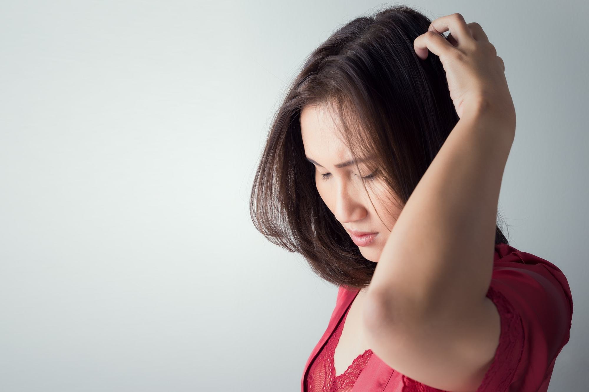 woman in red top touching and inspecting her scalp