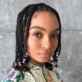 close up shot of yara shahidi with bob braids hairstyle with beads at the end, wearing floral dress and posing in a studio