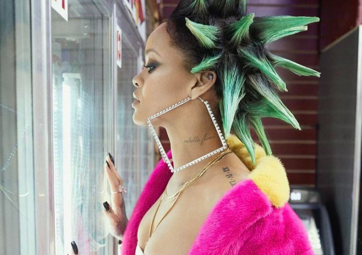 rihanna with hair styled into large spikes and coloured green, wearing large square earrings, and a neon pink and yellow fur coat