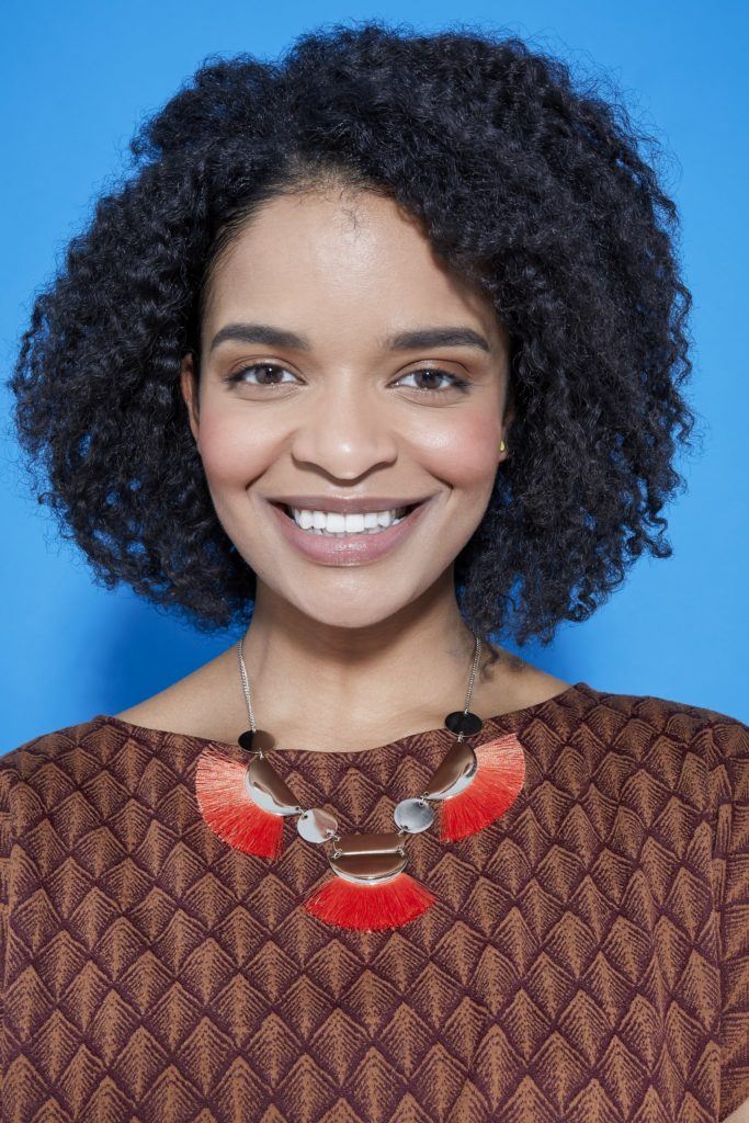 woman with natural curly hair in a bob length cut with a braid out style smiling at the camera