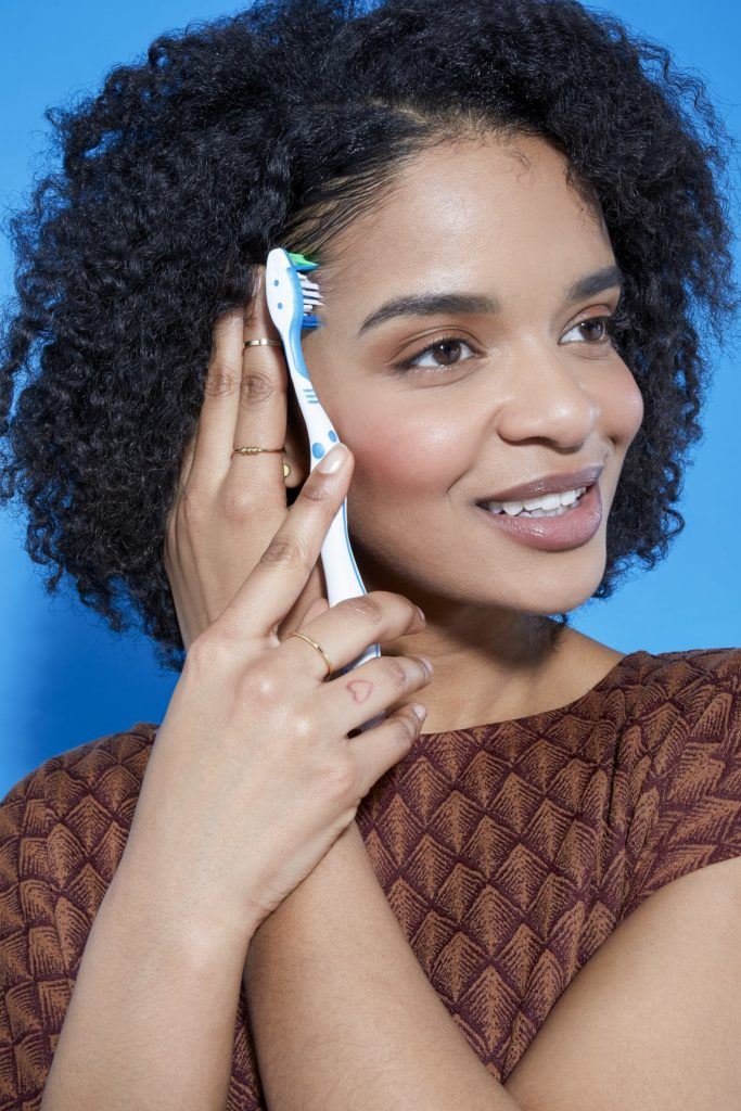 woman with natural curly hair in a bob length cut using a toothbrush to style her small front hairs down