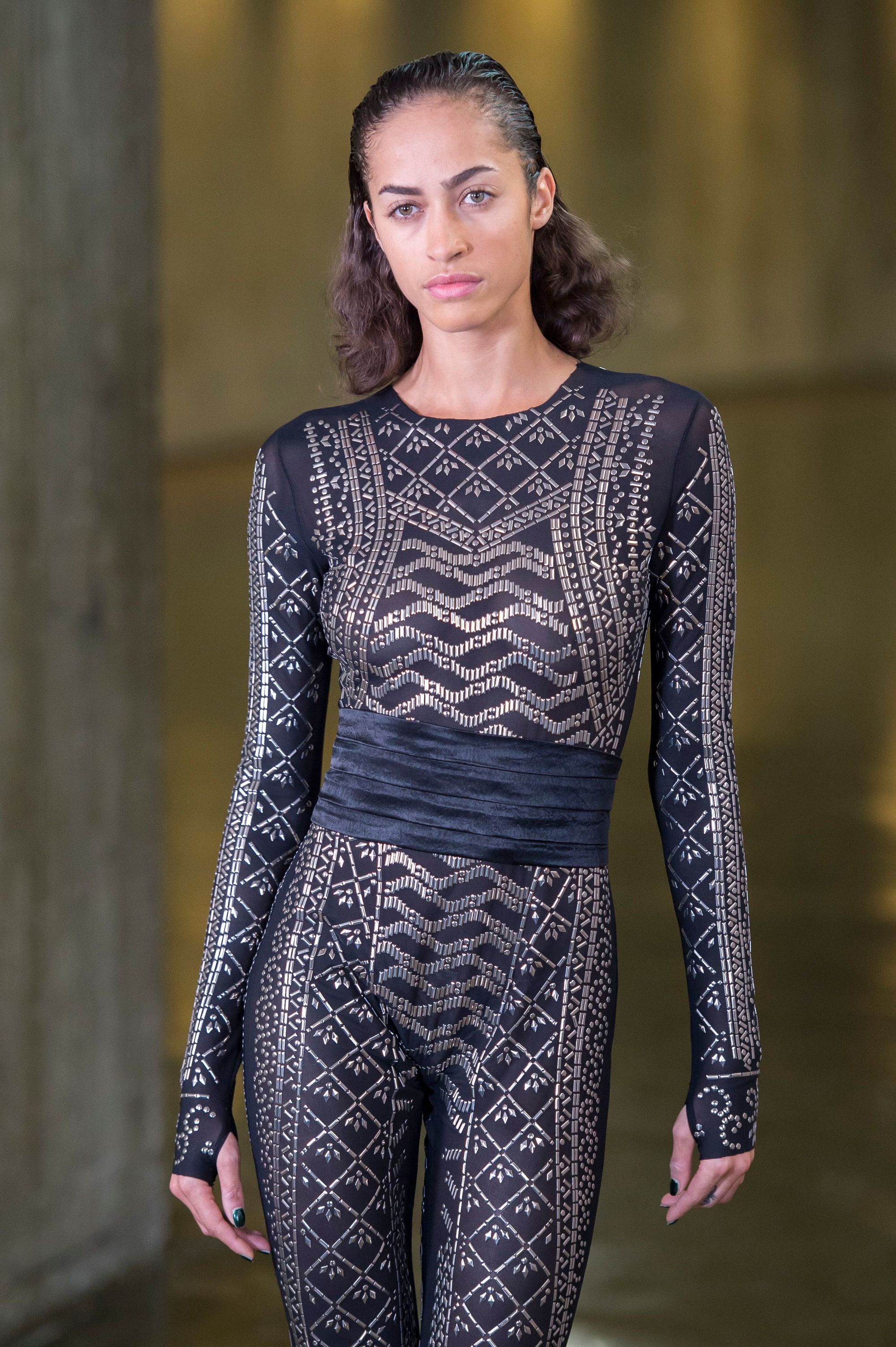 Easy hairstyles for short curly hair: Model with brown curly hair swept back wearing a cut out jumpsuit on runway.